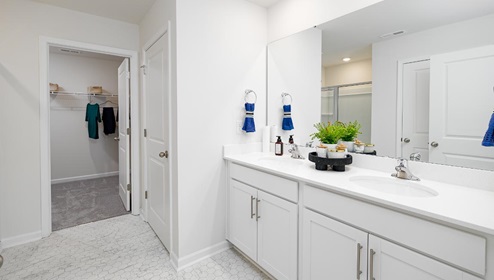 Fergus Crossing Penwell Model primary bathroom with double sinks, white counters and cabinets, and view of walk in closet