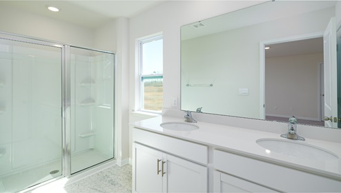 Primary bathroom with double sinks, white counters and cabinets, glass door shower