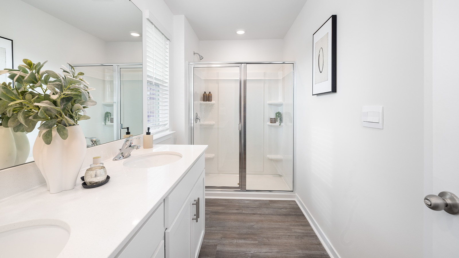 Primary bathroom with double sinks, white counters and cabinets, glass door shower