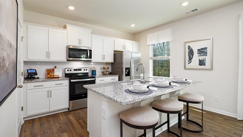 Fergus Crossing Penwell Model kitchen and island with white cabinets, wood floors and stainless steel appliances