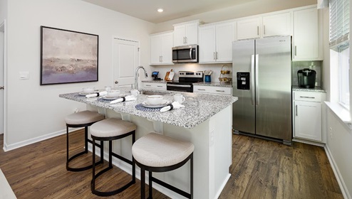 Fergus Crossing Penwell Model kitchen and island with white cabinets, wood floors and stainless steel appliances