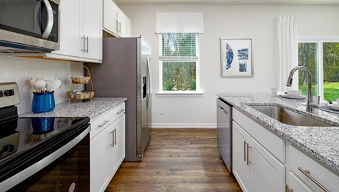 Fergus Crossing Penwell Model kitchen and island with white cabinets, wood floors and stainless steel appliances