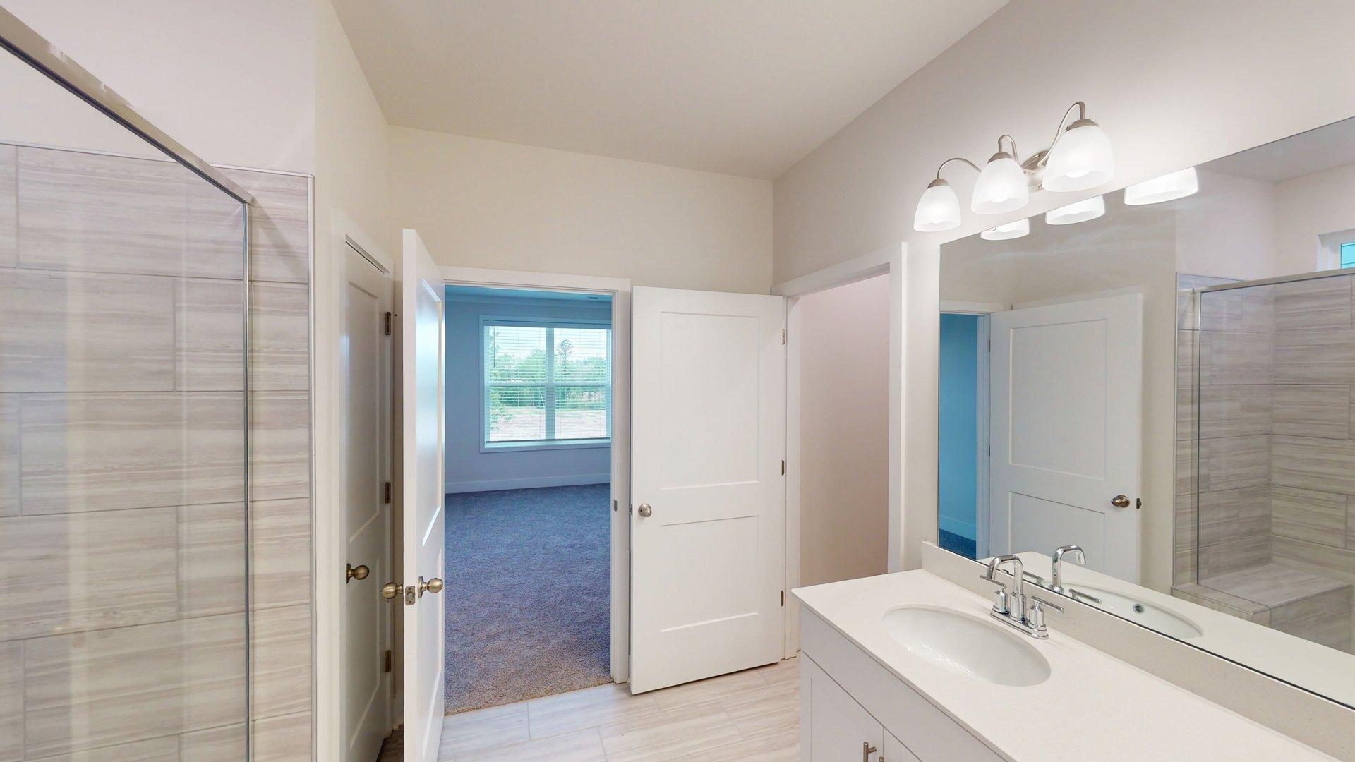 Primary bathroom with grey cabinets, white countertop, double sink vanity and glass door shower. New Homes in Charlotte, North Carolina