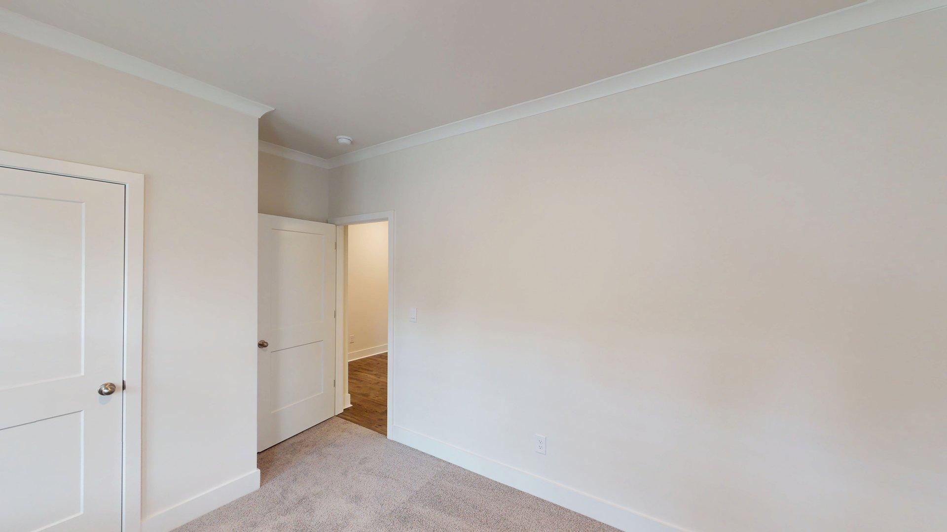 Carpeted bedroom with small window. Primary bathroom with grey cabinets, white countertop, double sink vanity and glass door shower. New Homes in Charlotte, North Carolina