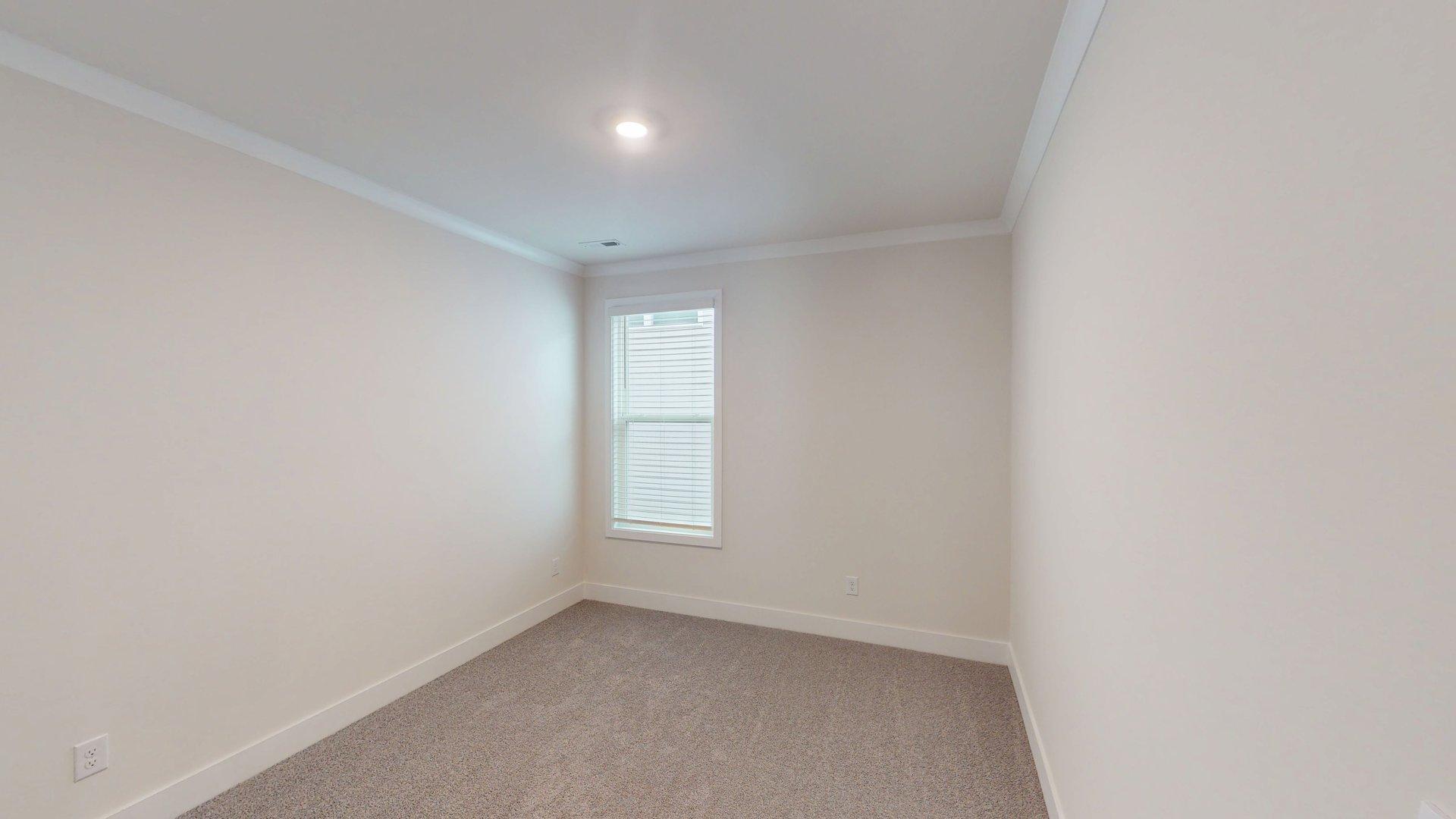 Carpeted bedroom with small window. Primary bathroom with grey cabinets, white countertop, double sink vanity and glass door shower. New Homes in Charlotte, North Carolina
