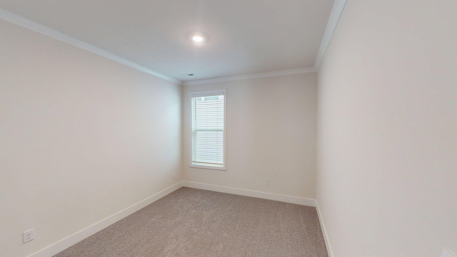 Carpeted bedroom with small window. Primary bathroom with grey cabinets, white countertop, double sink vanity and glass door shower. New Homes in Charlotte, North Carolina