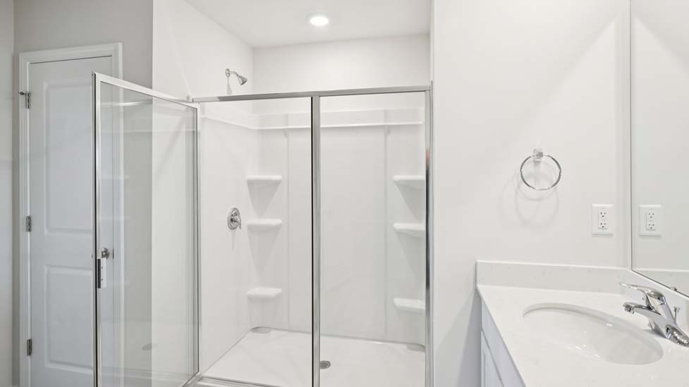 Primary bathroom with double sinks, white counters, and cabinets, glass door shower