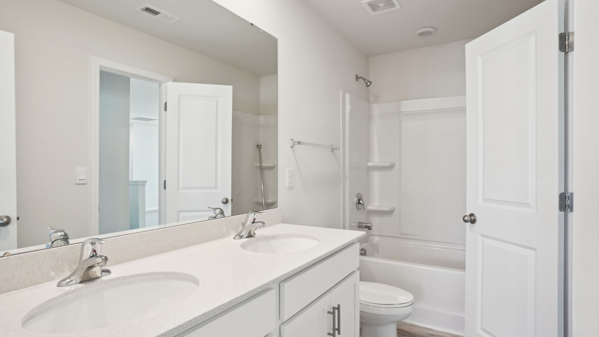 Primary bathroom with double sinks, white counters, and cabinets, glass door shower