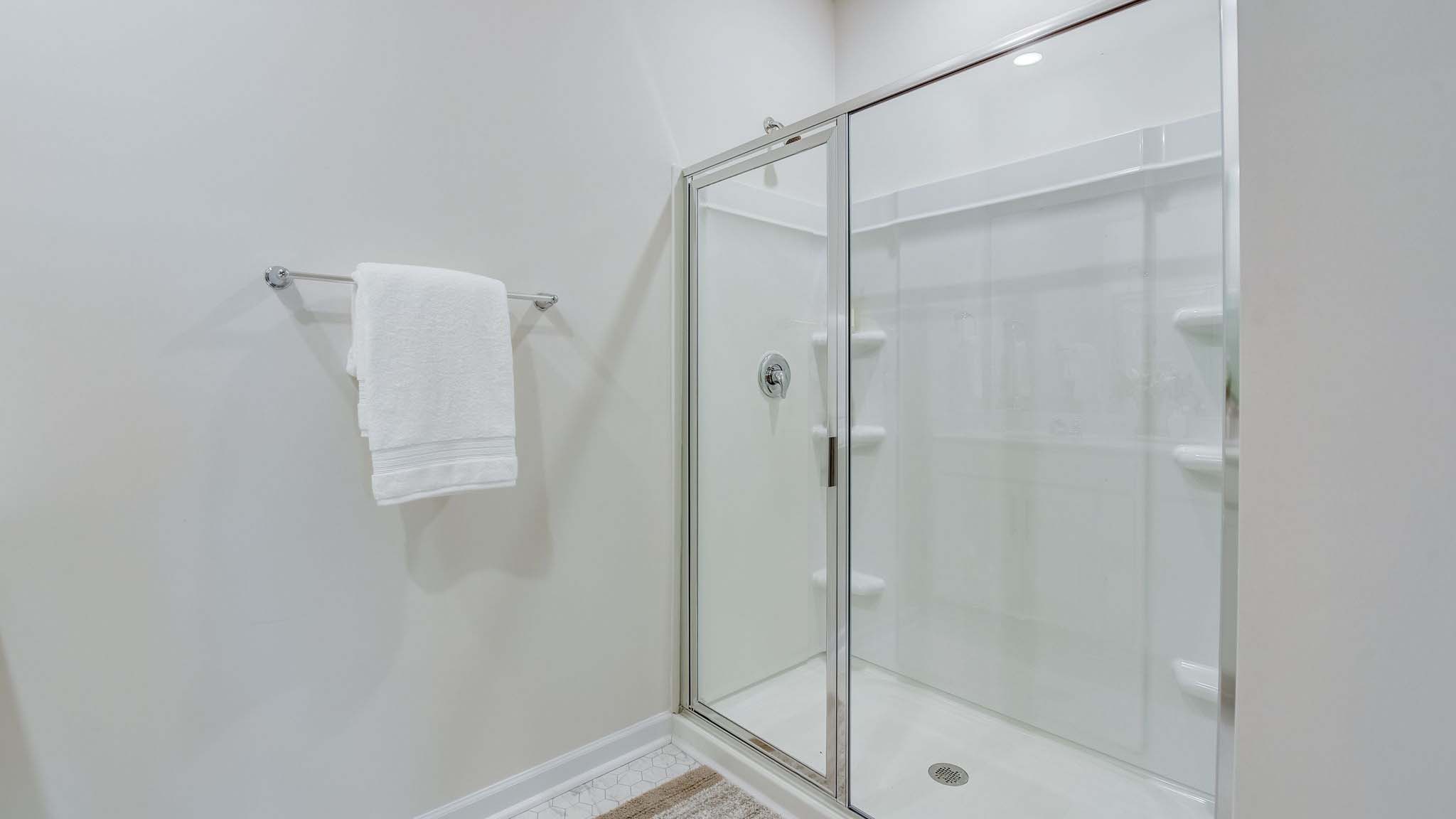 Primary bathroom with double sinks, white cabinets and counters, and glass door shower