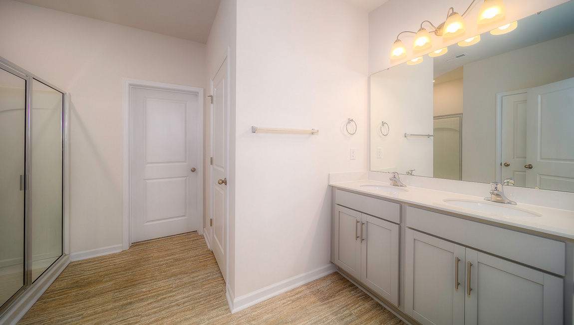 Primary bathroom with double sinks, standing glass shower, and toilet
