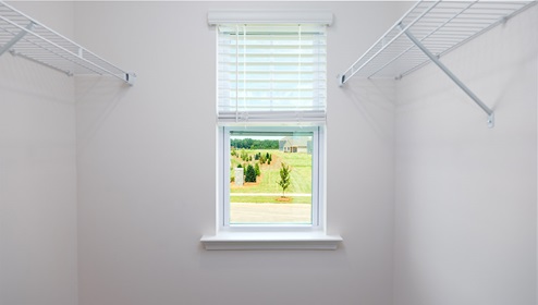 Primary bedroom walk in closet with carpet and hanging racks and small window