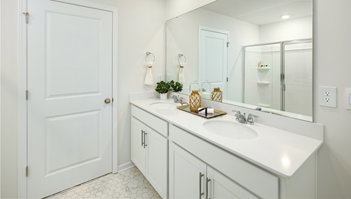 Primary bathroom with double sinks, white cabinets and counters, and glass door shower
