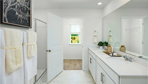 Primary bathroom with double sinks, white cabinets and counters, and glass door shower