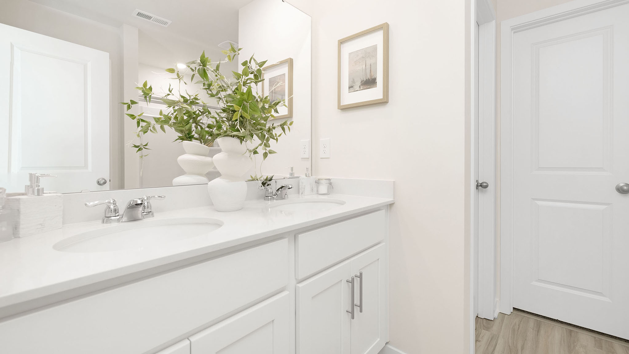 Primary bathroom with white counters and cabinets, double sinks and glass door shower