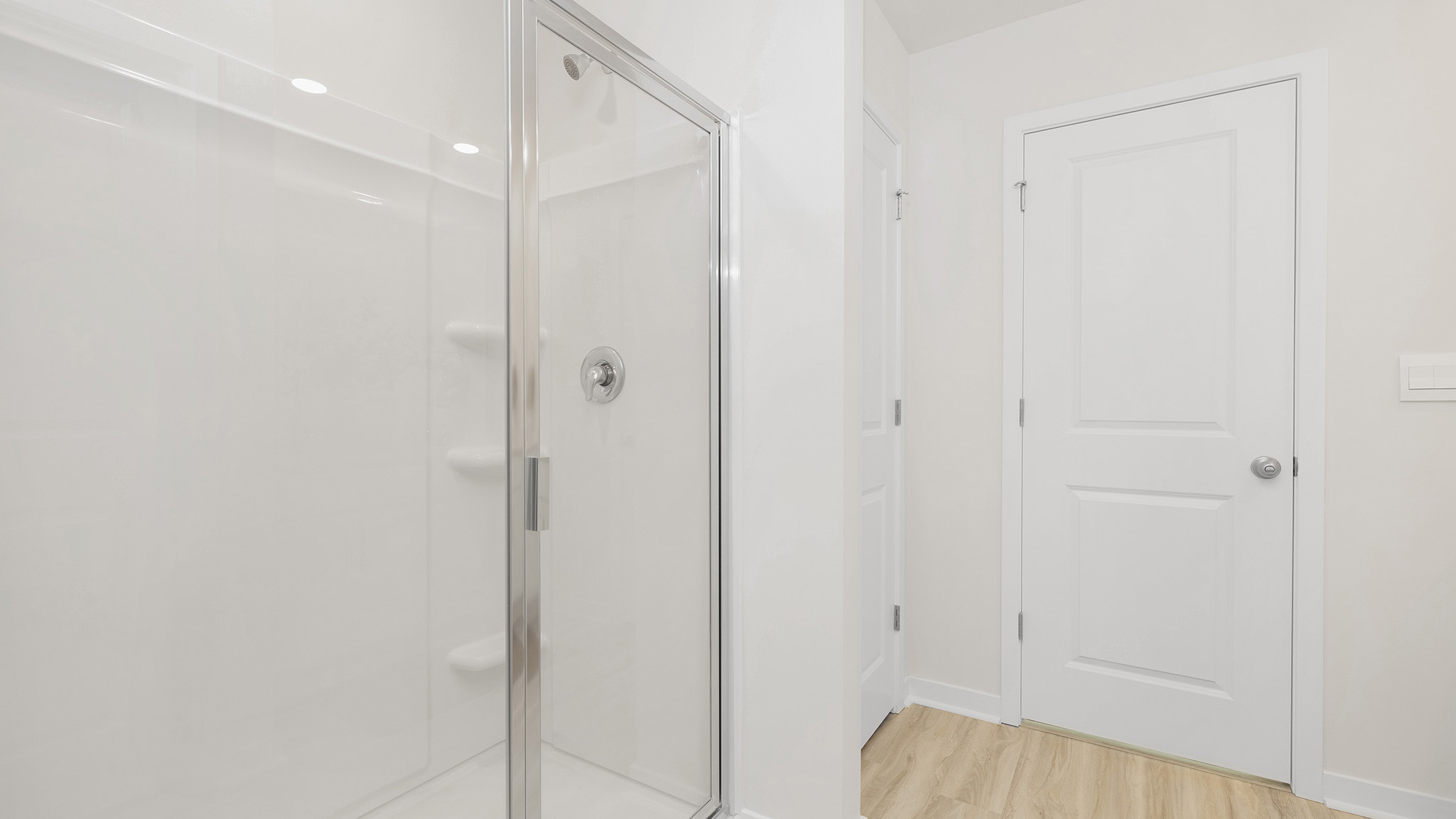 Primary bathroom with white counters and cabinets, double sinks and glass door shower