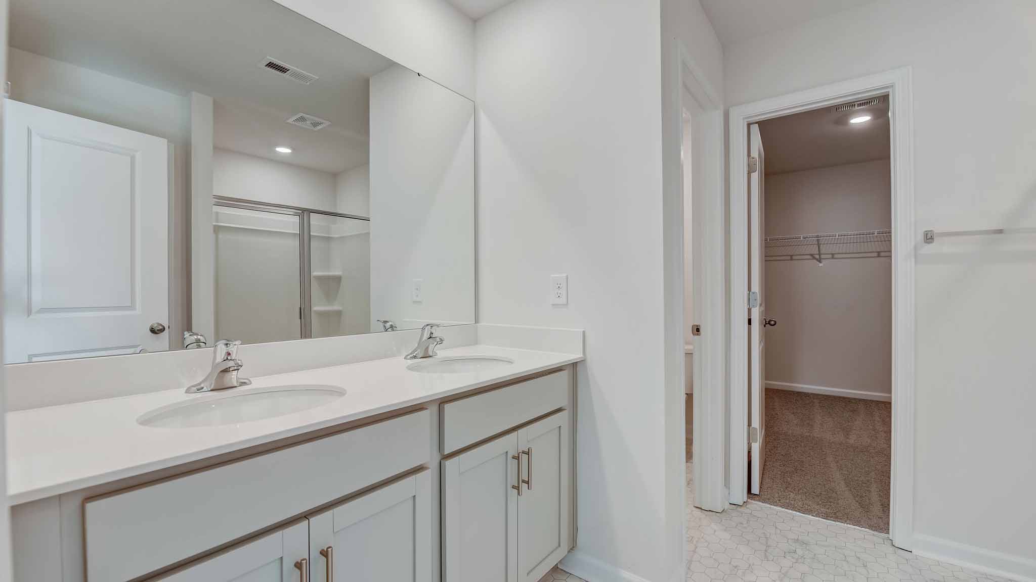 Primary bathroom with white counters and cabinets, double sinks and glass door shower