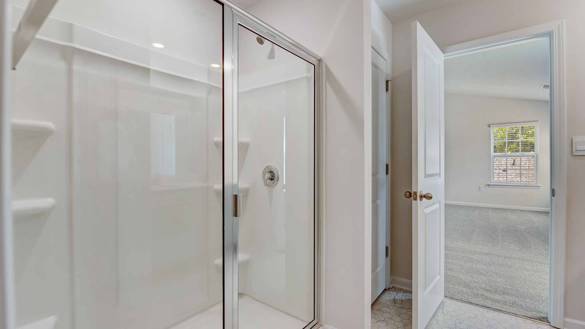 Primary bathroom with white counters and cabinets, double sinks and glass door shower