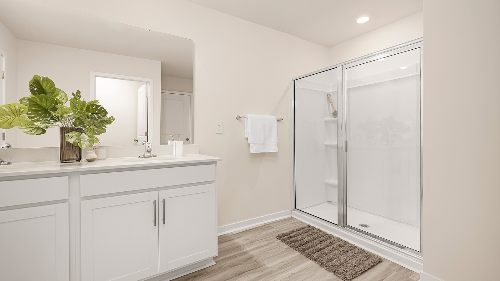 Primary bathroom with double sinks, white cabinets and glass door shower