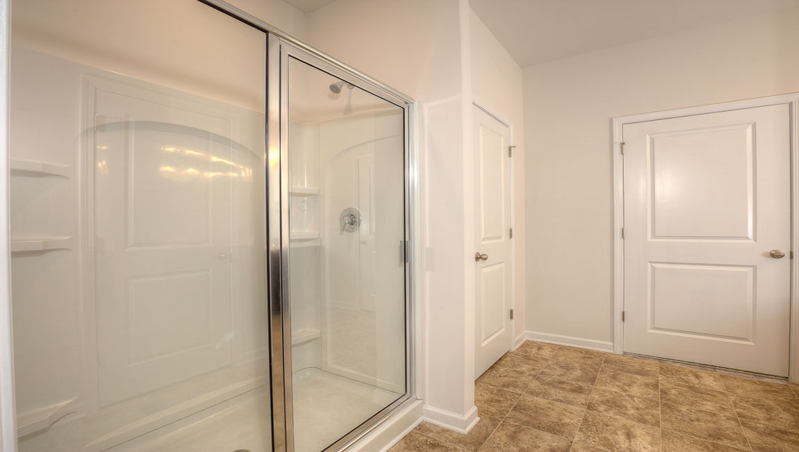 Primary bathroom with double sinks, standing glass shower, and toilet