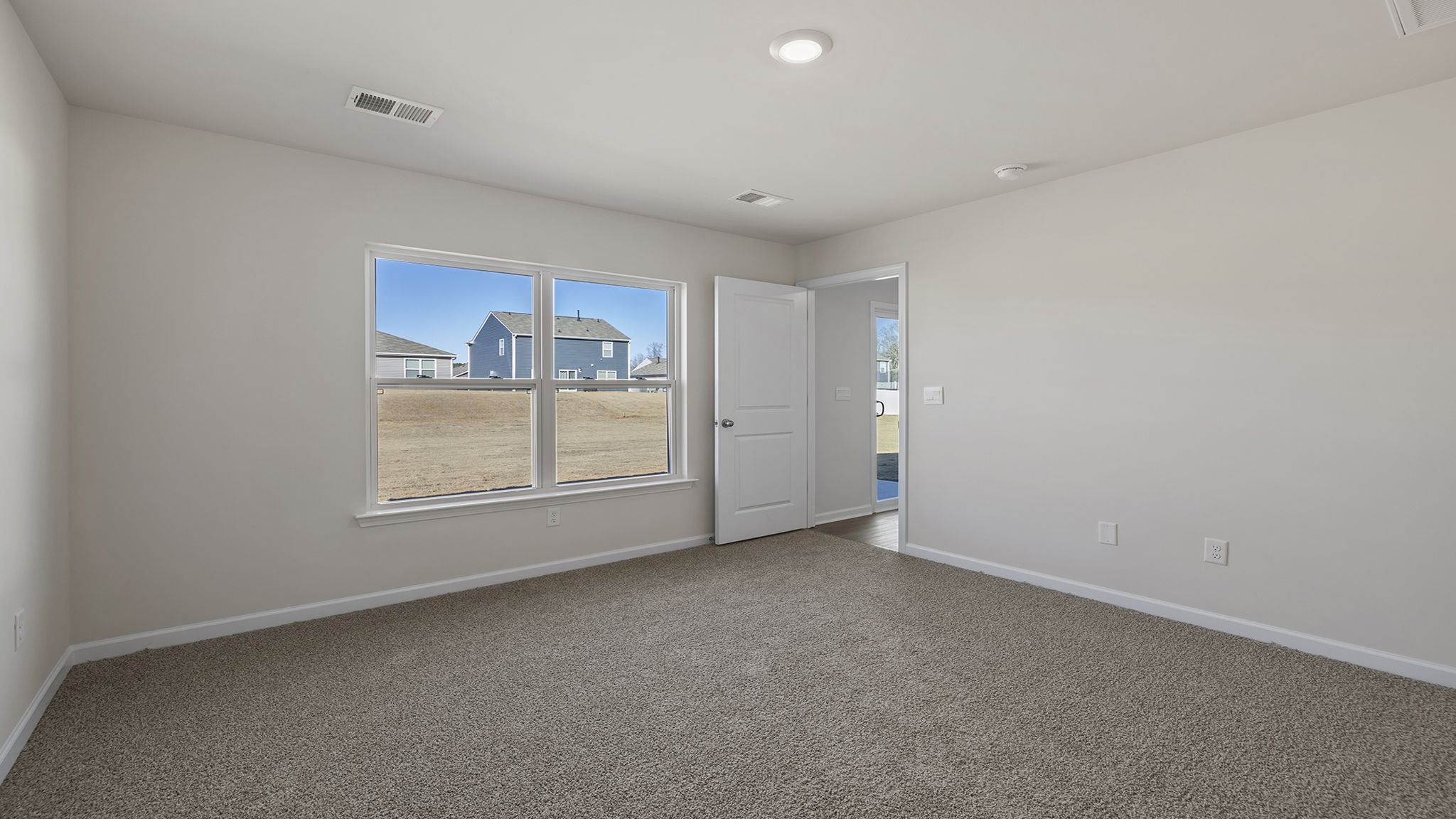 Primary bedroom off the dining room with large window and carpet.