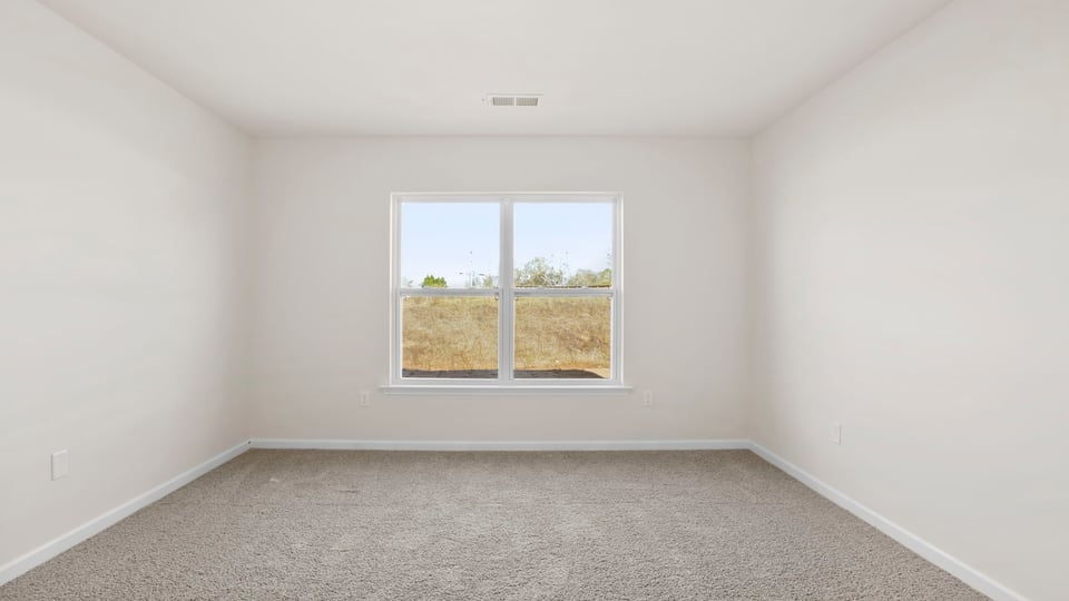 Primary bedroom with carpet and window.