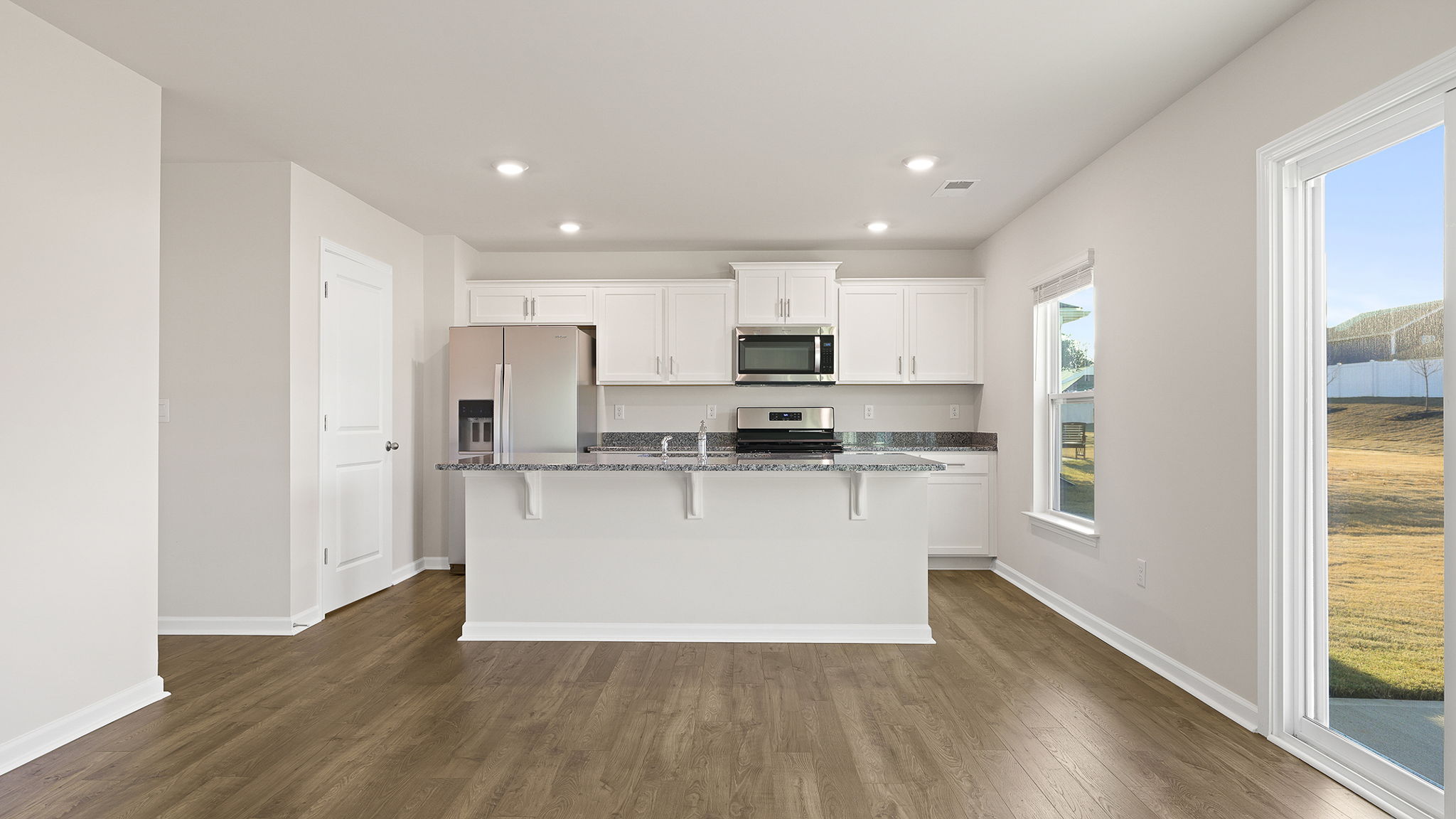 View of island, refrigerator opening, recessed lighting and cabinetry.