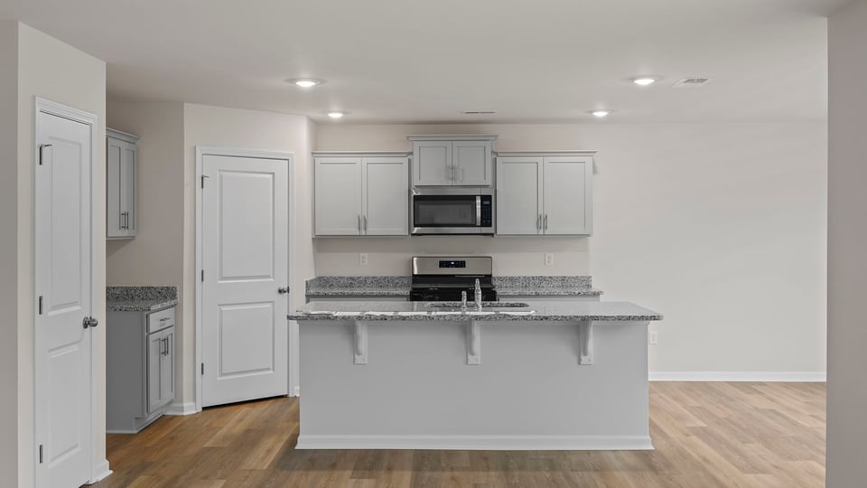 View of kitchen with island, quartz countertops, stainless steel appliances and white cabinetry.