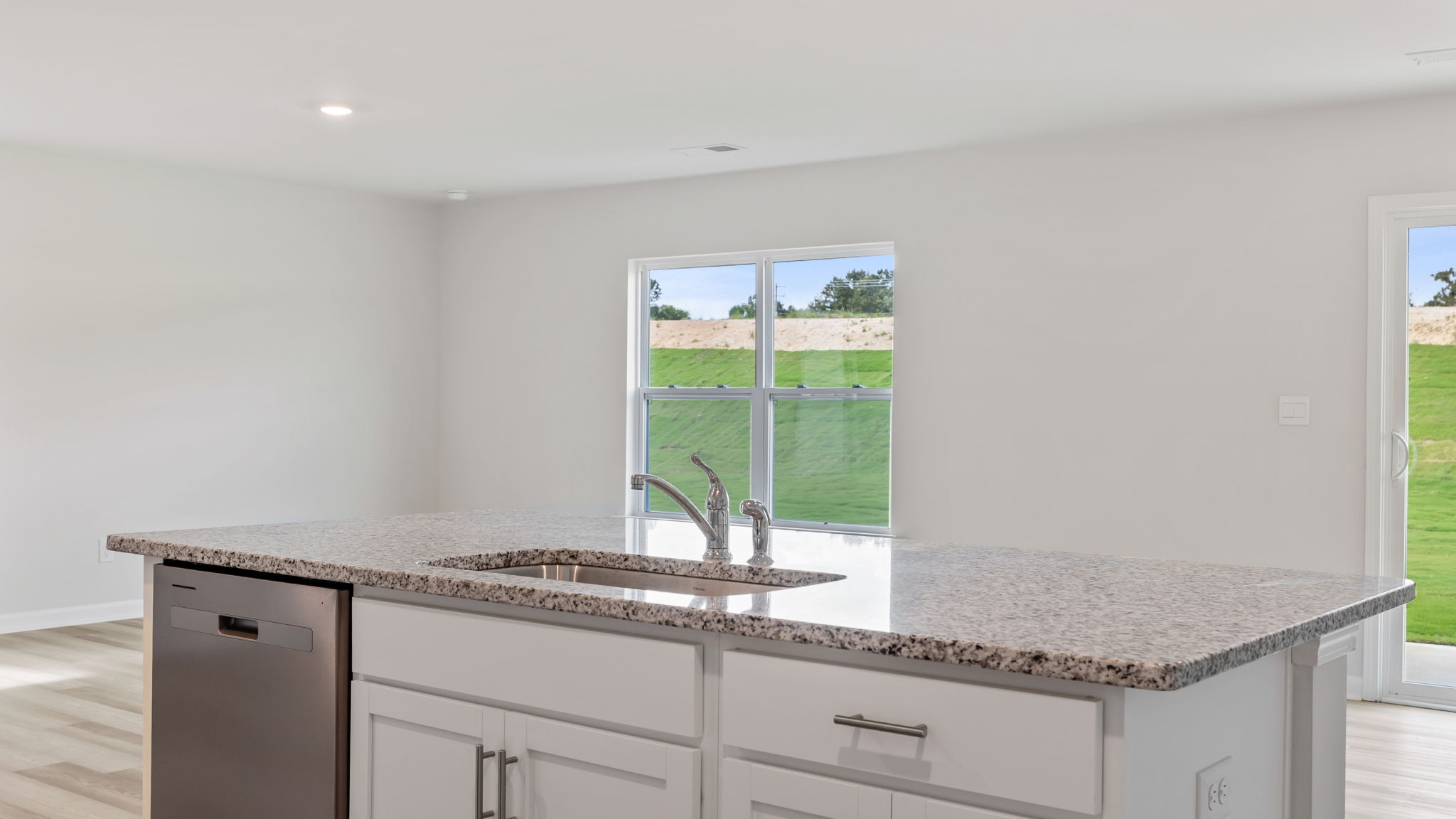 Kitchen island with quartz countertop hosts the sink and dishwasher overlooking the dining area and door to the back yard.