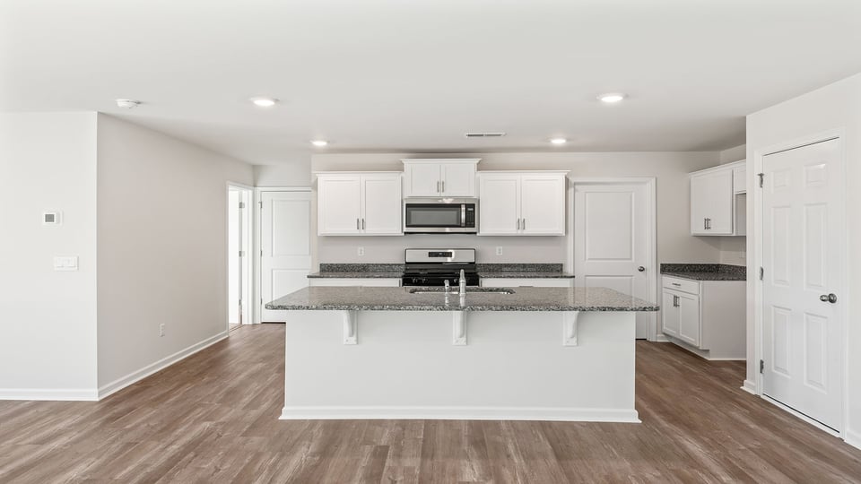 Open kitchen with recessed lighting, quartz countertops, white cabinetry.