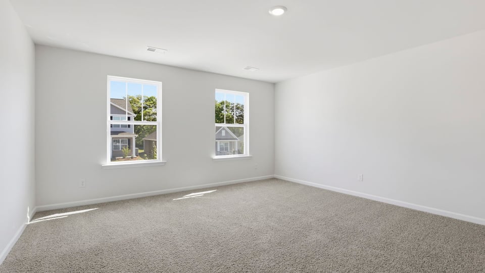 Primary bedroom with carpet and windows.