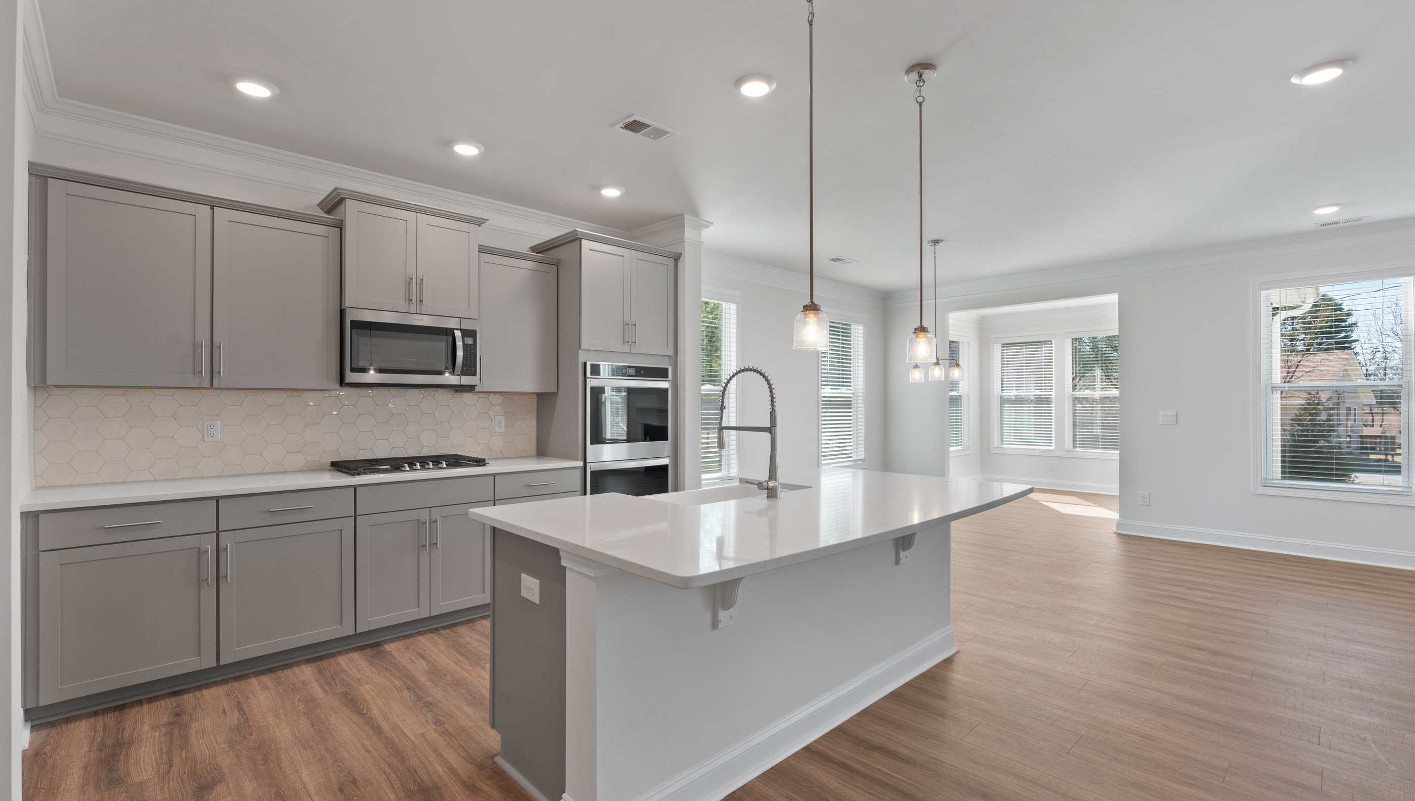 View of gourmet kitchen with quartz center island, stainless steel appliances, and recessed and pendulum lighting.