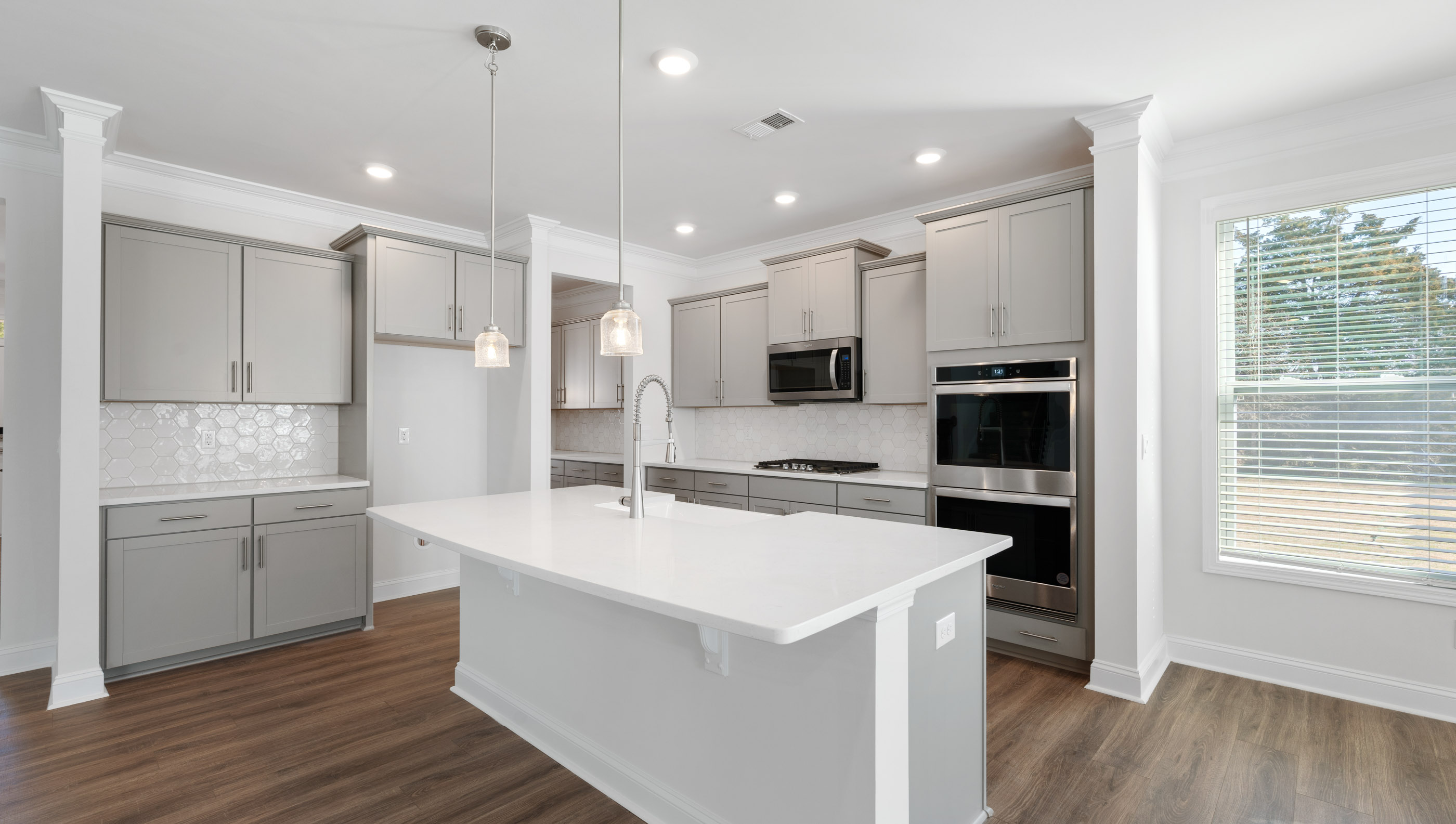 View of gourmet kitchen with quartz center island, stainless steel appliances, and recessed and pendulum lighting.