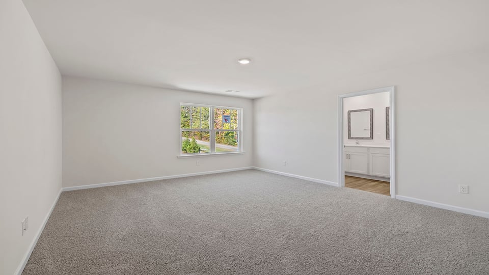 View of primary bedroom with large window and entrance into primary bath.