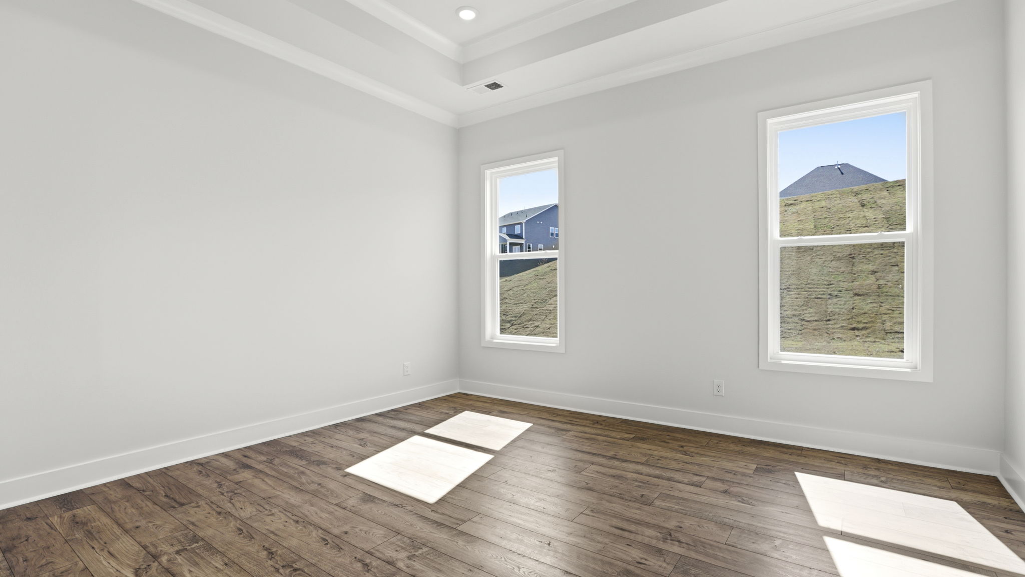 Primary bedroom on main level with trey ceiling and two large windows.