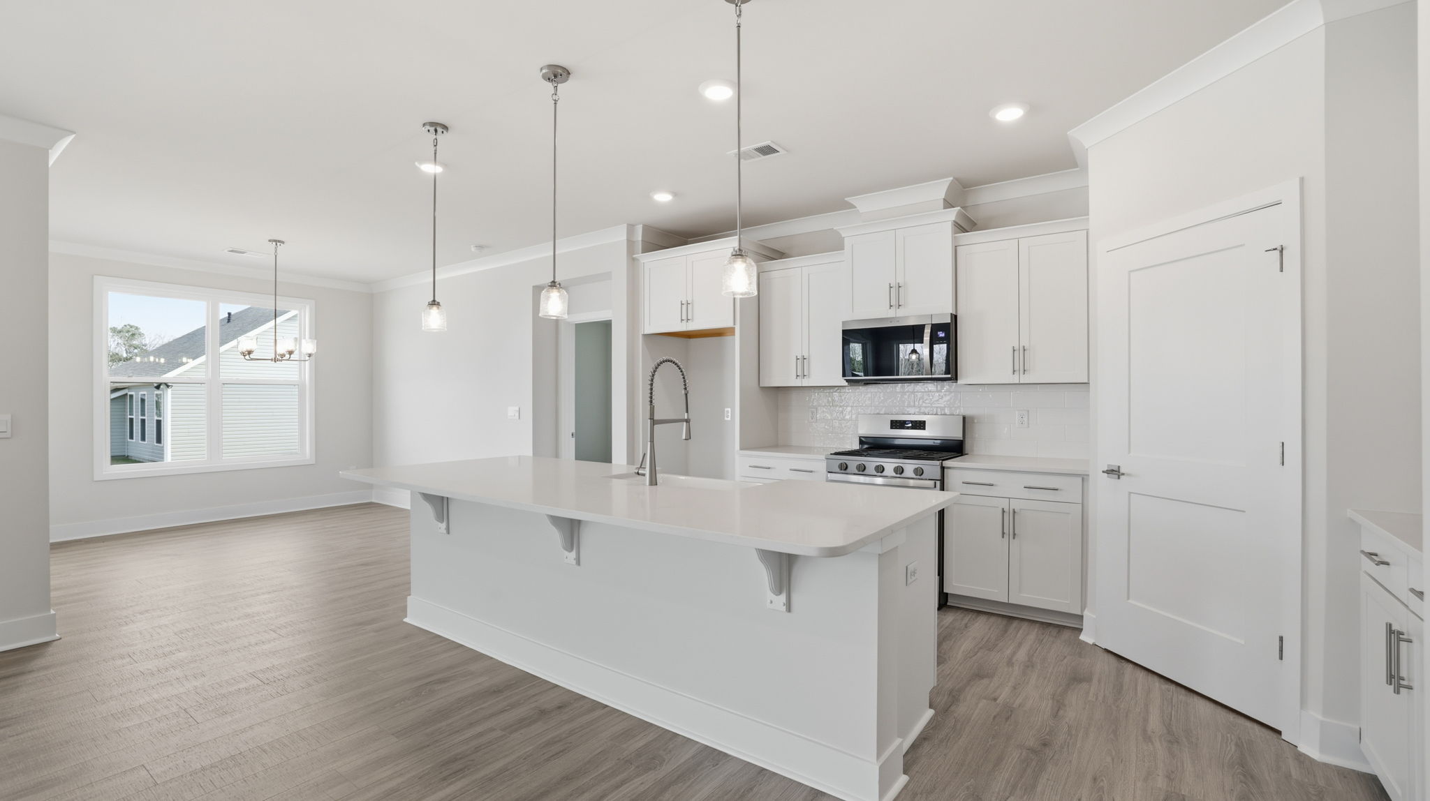 View of the kitchen with island, pendulum lighting, stainless steel appliances, and open to the dining room.