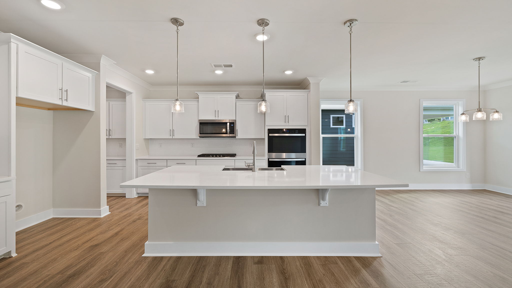 View of gourmet kitchen with quartz center island, stainless steel appliances, and recessed and pendulum lighting.
