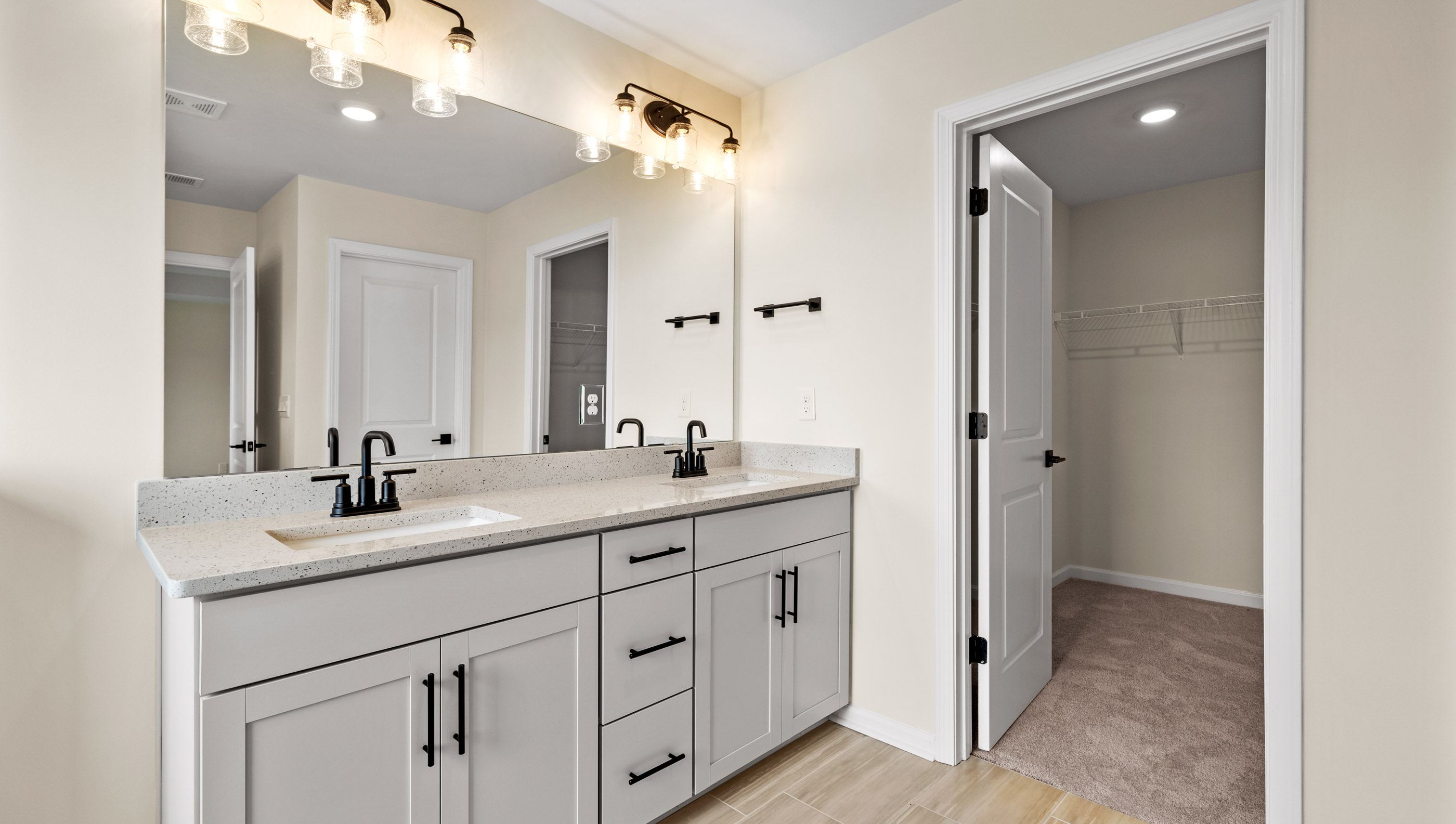 Primary bathroom with double vanities and closet view.