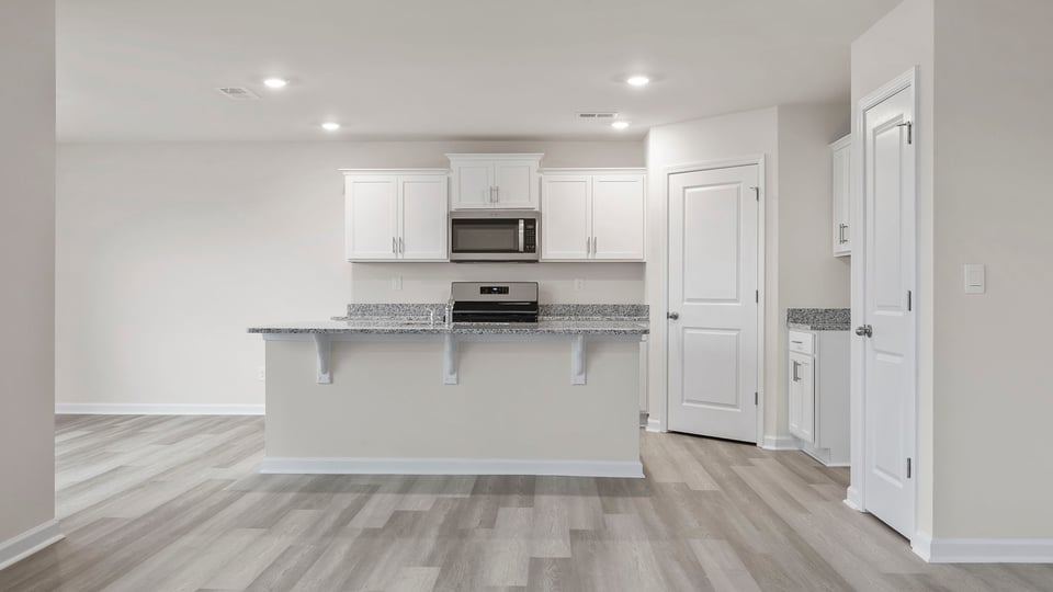 View of kitchen with island, quartz countertops, stainless steel appliances and white cabinetry.