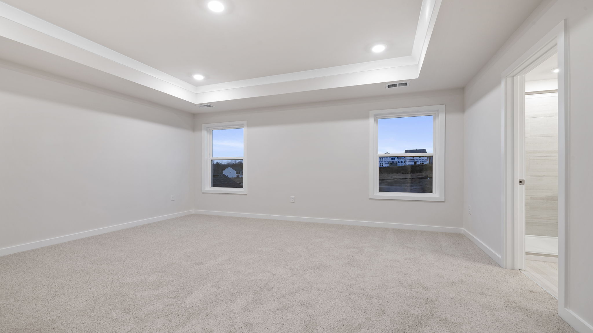Primary bedroom with carpet, trey ceiling and windows.