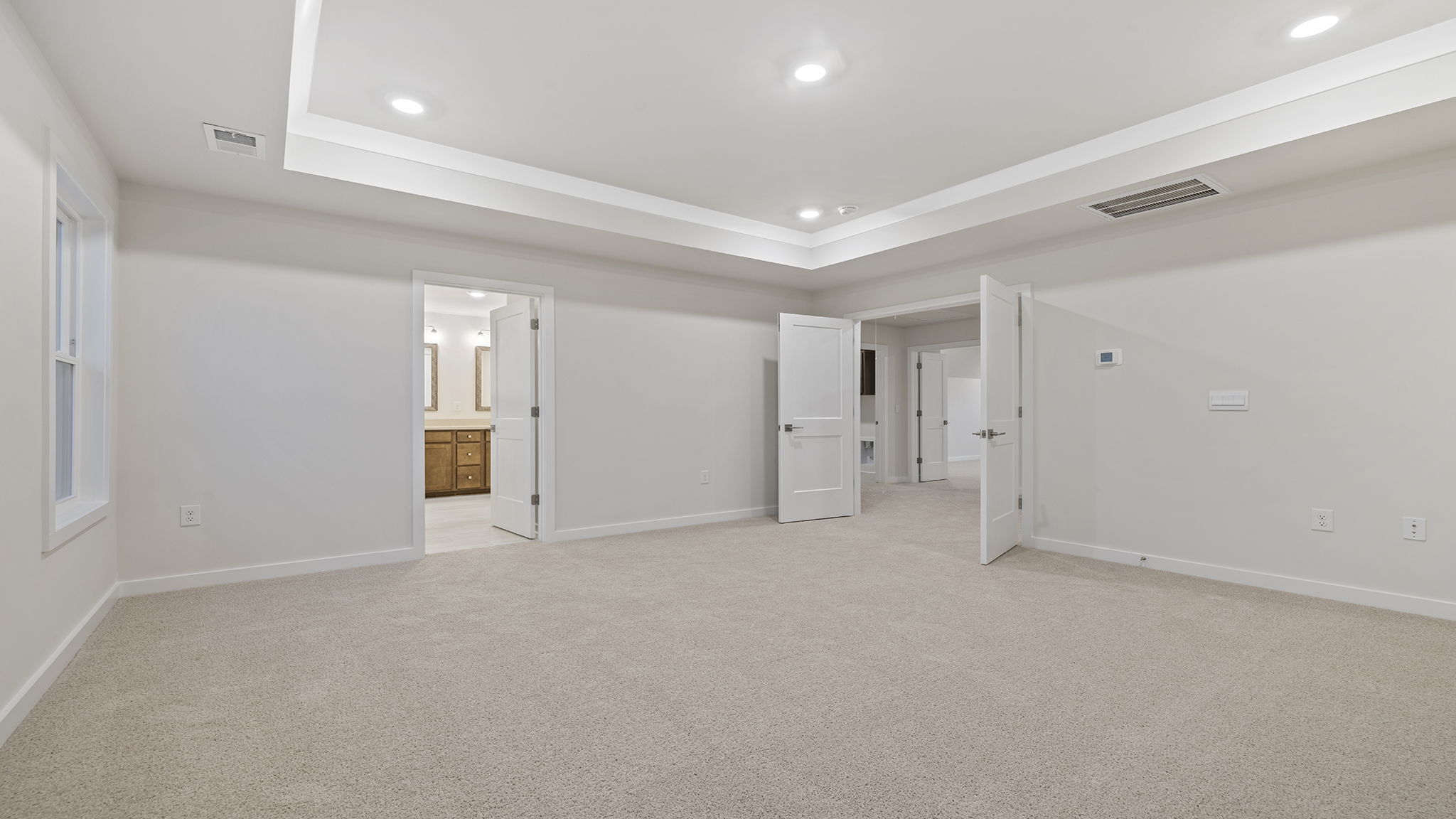 Primary bedroom with carpet, trey ceiling and windows.