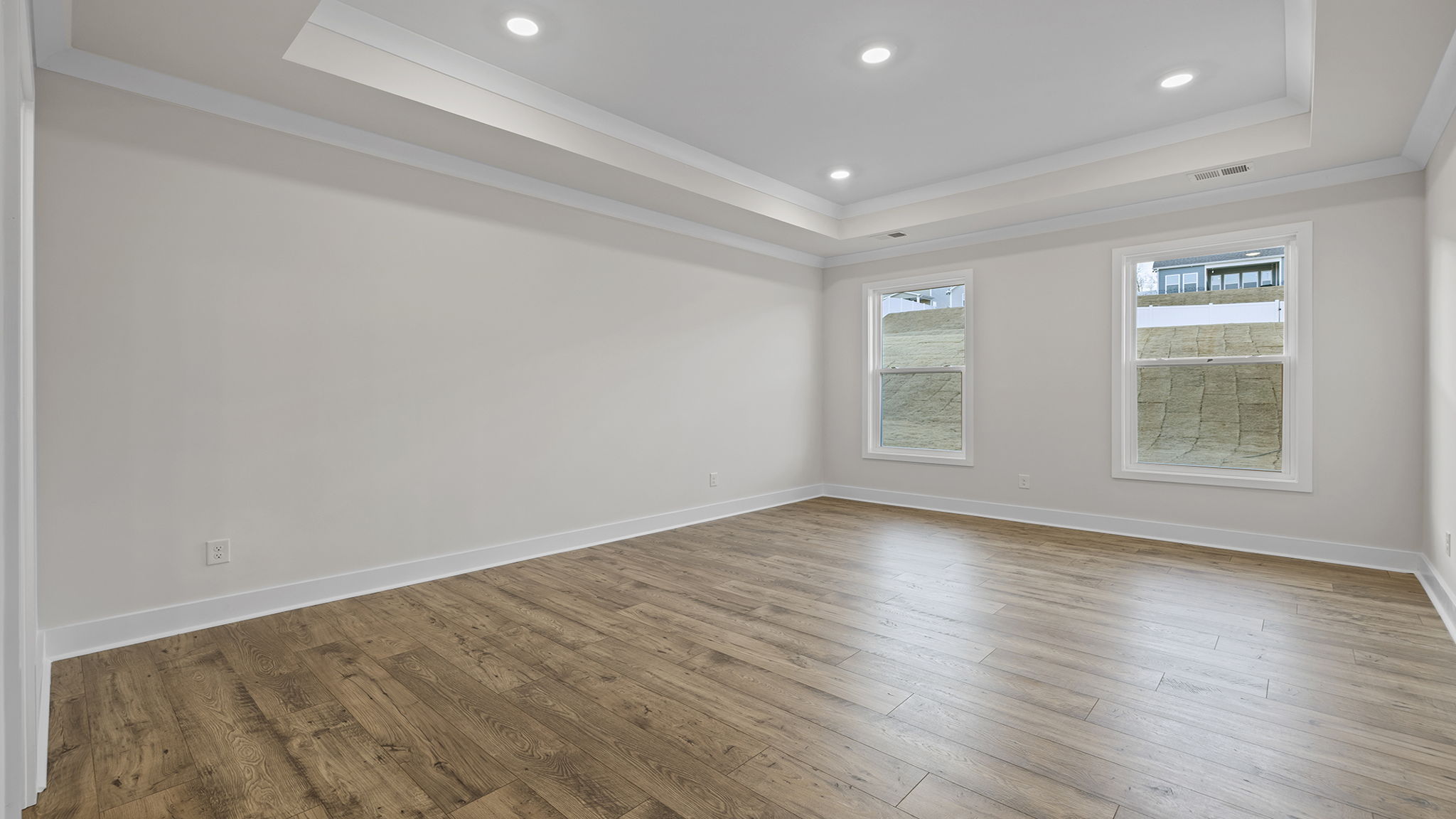 Primary bedroom on the main level with two large windows, trey ceiling and recessed lighting.