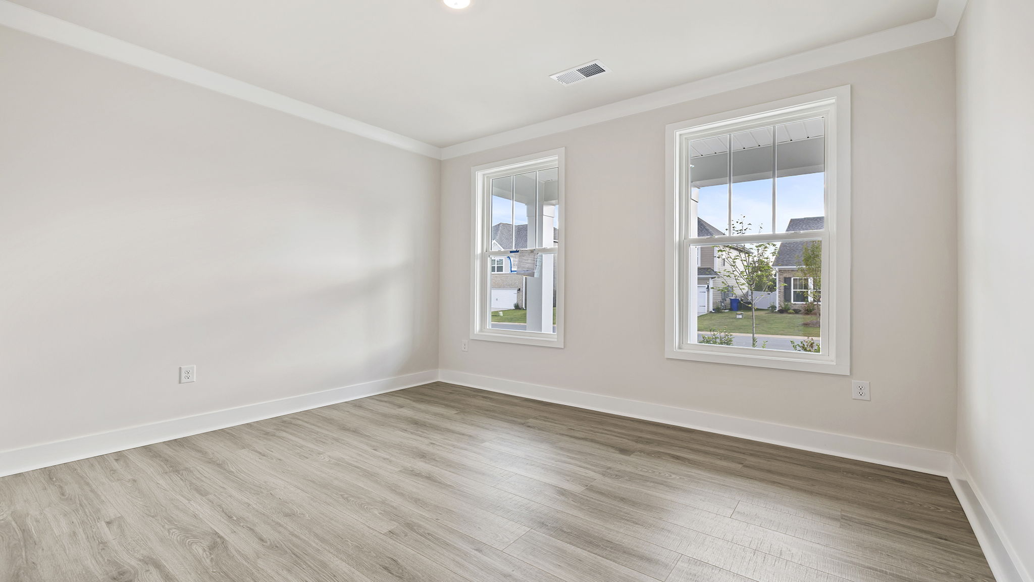 Bedroom with two large windows and laminate flooring.