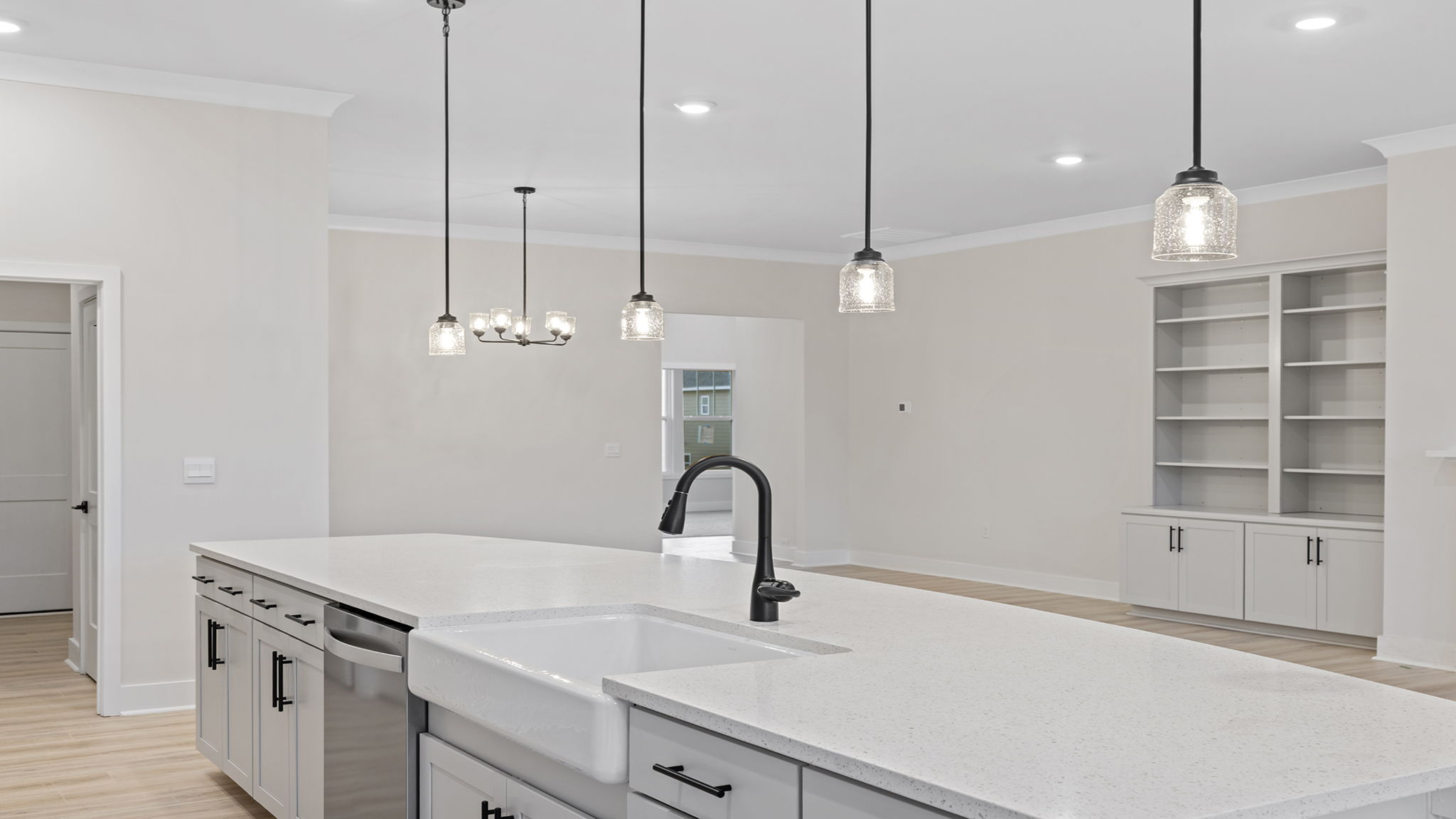 Kitchen island hosts sink and dishwasher and accented by pendulum lighting.