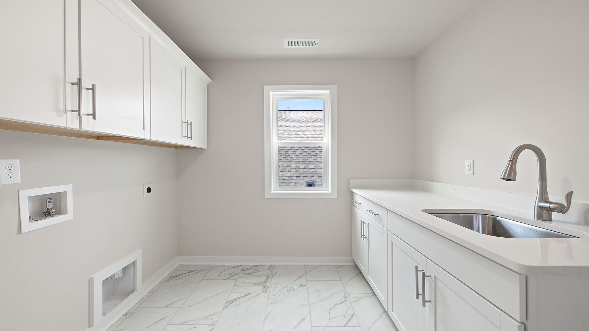 View of laundry room with cabinets and sink with quartz countertop and storage.