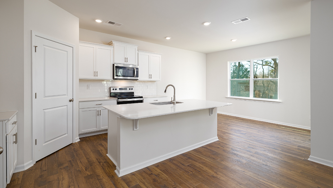 Kitchen and island with white cabinets, quartz counters, wood floors and stainless steel appliances