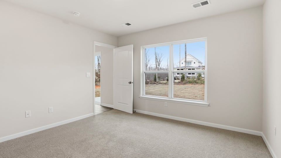Primary bedroom off the living area with large windows and carpet.