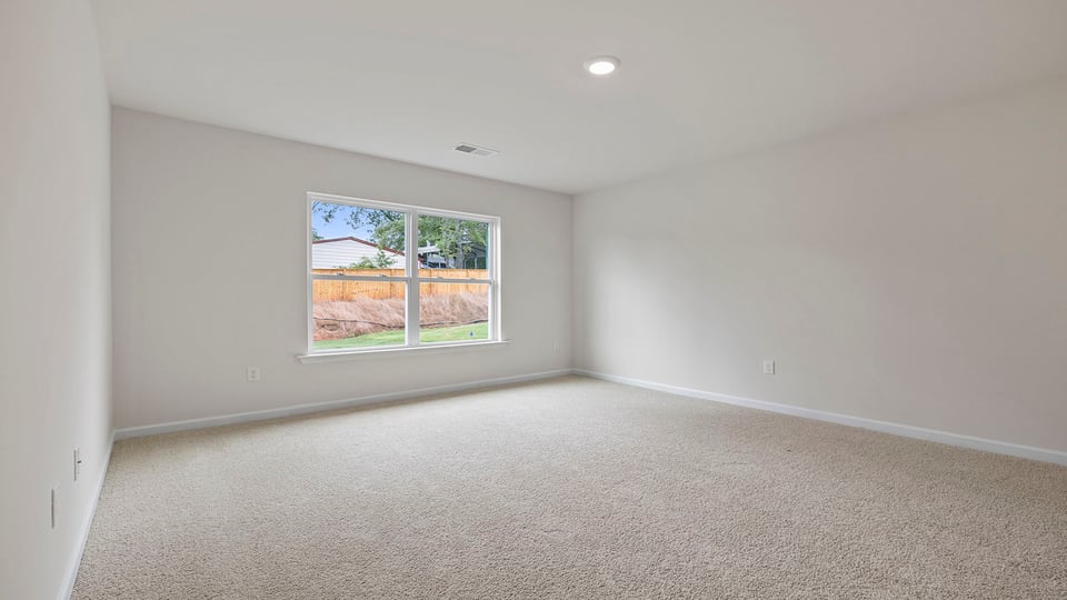 Primary bedroom with carpet and window.