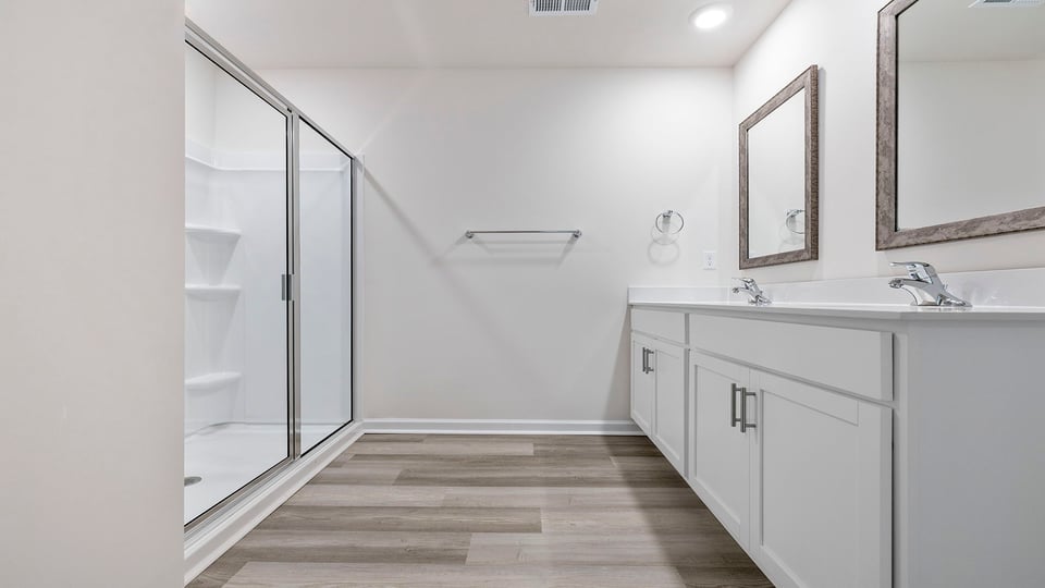 Primary bathroom with dual sink vanity and mirrors, and large walk-in shower.