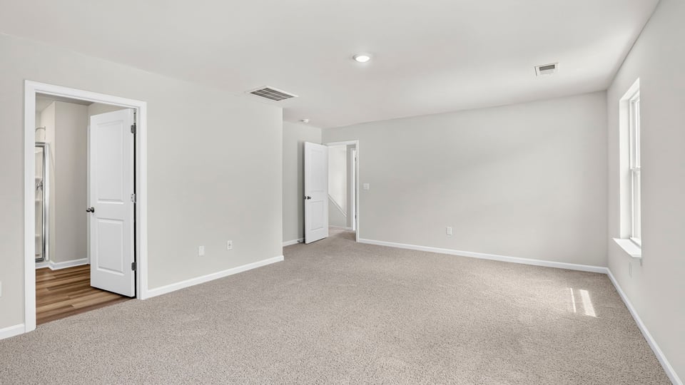 Primary bedroom with carpet and windows.