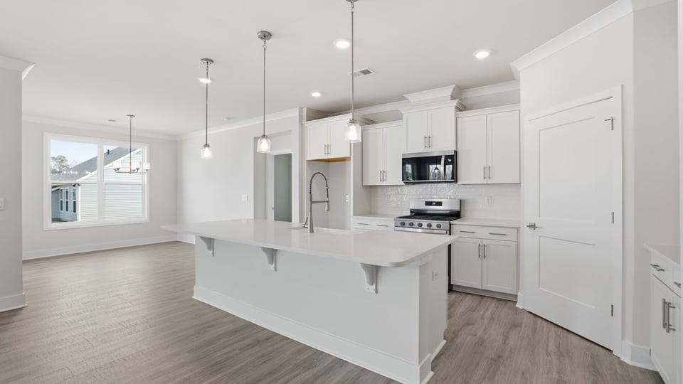 View of the kitchen with island, pendulum lighting and open to the dining room.